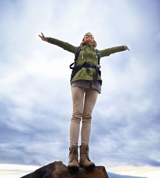 In the spirit of adventure. A young woman standing with her arms outstretched on a cliff.