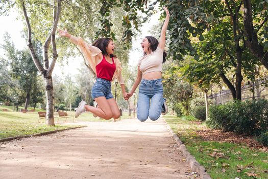 two young women jumping with joy holding hands