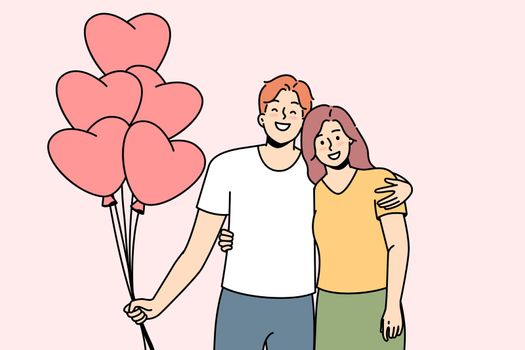 Smiling couple hug holding heart shaped balloons