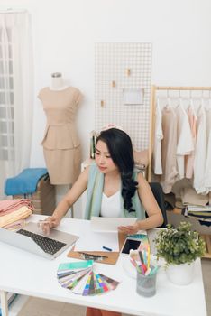 Pretty young casual businesswoman sitting in front of laptop in workshop or studio and searching for new ideas in the net