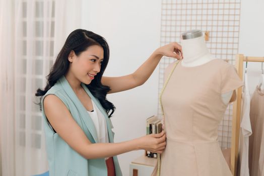 An Asian girl  is working in the workshop studio. She makes fitting on the dress on the mannequin.