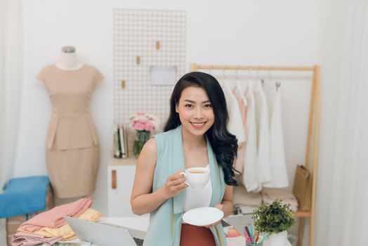 Portrait of beautiful young Asian fashion designer businesswoman at her studio while drinking coffee