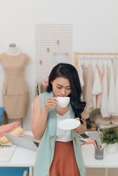 Happy young Asian fashion designer business drinking coffee at her workshop/store