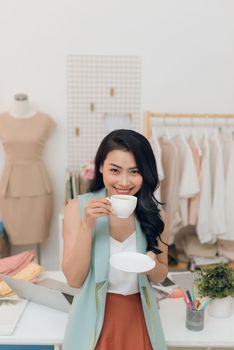 Young fashion designer on her atelier making a pause and drinking coffee