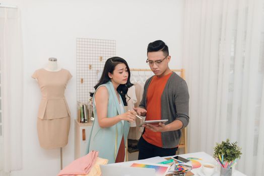 Two young woman and man fashion designers working and using tablet together at the studio
