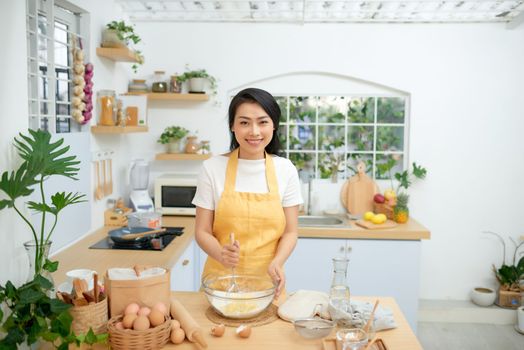 female mixing flour with eggs while using whisk. She is cooking bakery in domestic atmosphere