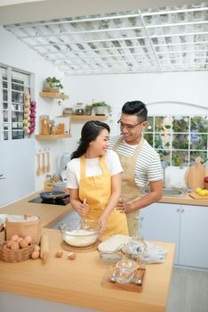 Couple man and woman wearing aprons having fun while making homemade pasta in kitchen at home