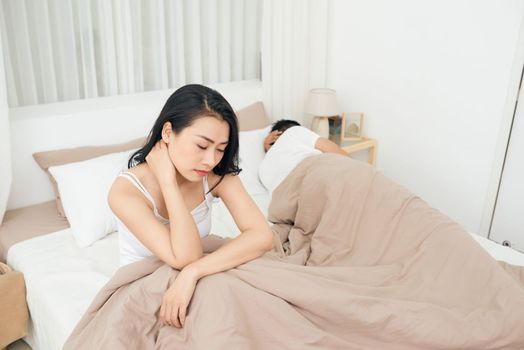 Unhappy Young Couple Sitting On Bed In Bedroom