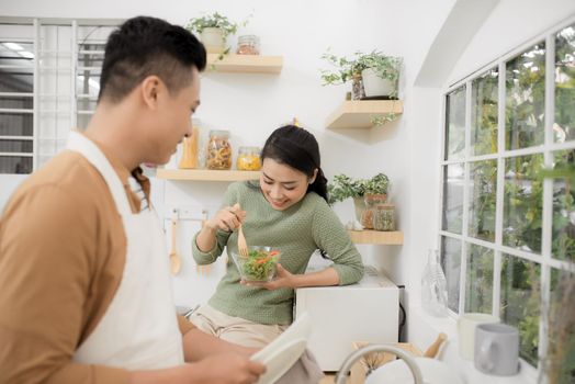 Loving woman feeding man while cooking dinner at kitchen.