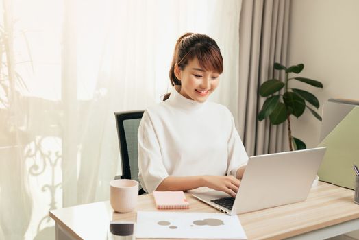 Cheerful young Asian woman working at home with computer 