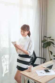 Young Asian woman writing notebook while standing behind working desk at home