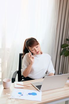 Asian Woman working on laptop at office while talking on phone