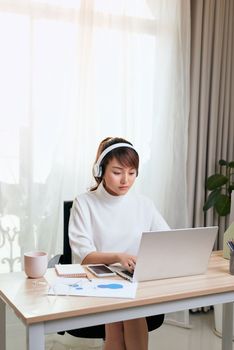 Young Asian businesswoman listening to music and working with laptop at home