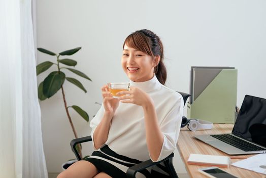 Beautiful Asian woman drinking while sitting at her office