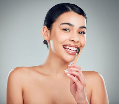 Studio portrait of a smiling mixed race young woman with glowing skin posing against grey copyspace background while brushing her teeth for fresh breath. Hispanic model using toothpaste to prevent a .