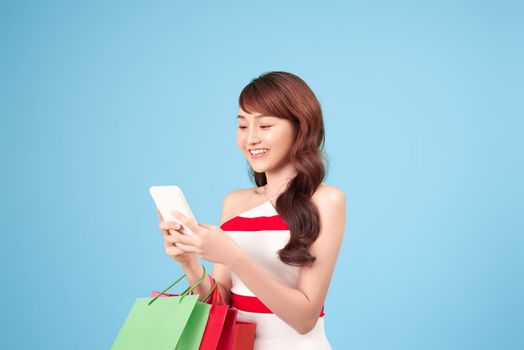 Beautiful young woman is using a smart phone for shopping online isolated on blue background studio