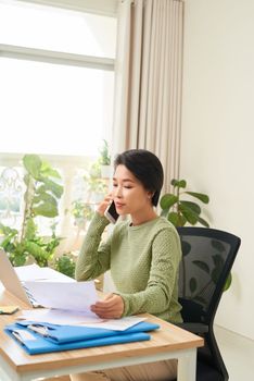 Woman working on laptop at home while talking on phone