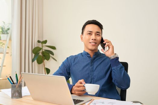 Smiling businessman sitting at working desk using typing on laptop, making answering call
