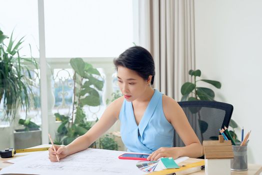 Asian female architect studying plans in office