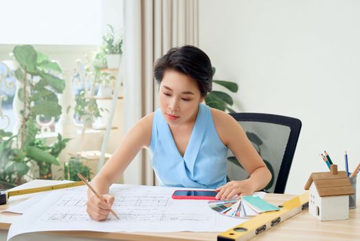 Asian female architect studying plans in office
