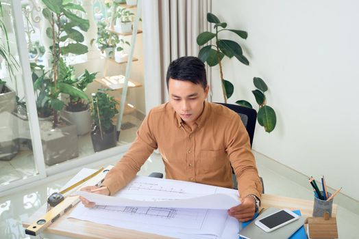 Young Asian Male Architect Studying Plans In Office
