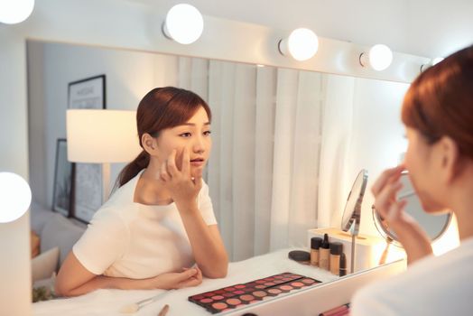Unhappy young Asian woman in front of a mirror looking at her wrinkles