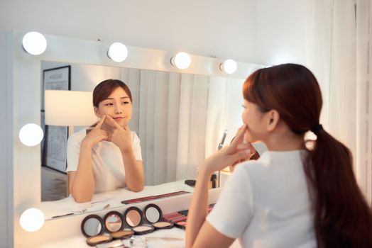Young Asian woman touching skin face in front of mirror.