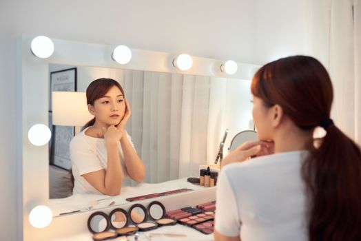 Young Asian woman taking care of her skin while looking in the morror