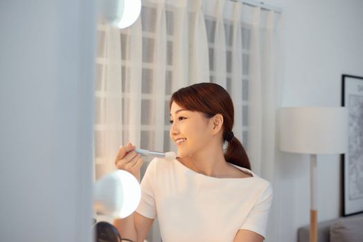 Young Asian woman apply blush on a cheekbone with a brush
