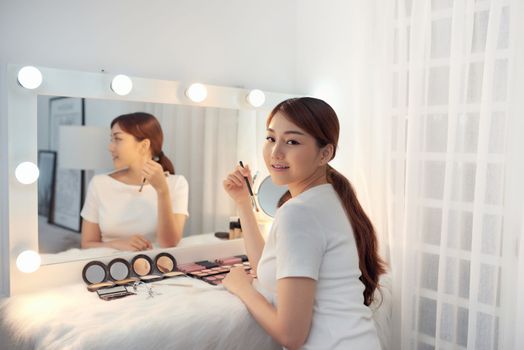 Beautiful Asian girl looking in the mirror and applying cosmetic with a brush