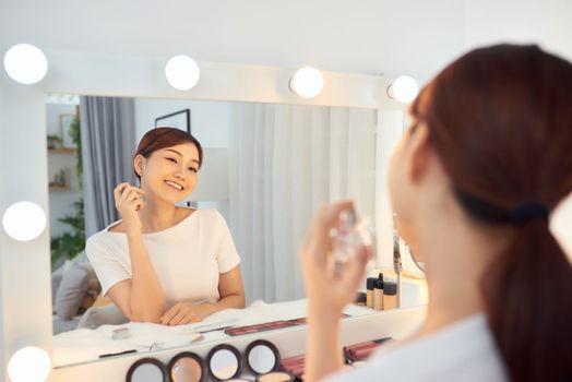 Asian Woman applying fragrance with a spray in front of a make up mirror
