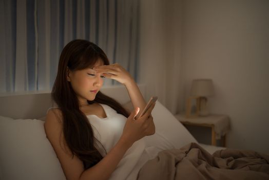 Disappointed sad woman holding mobile phone while lying on bed at night