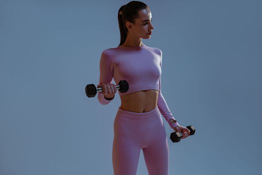 Fitness woman doing exercises with dumbbells on studio background and looking at side
