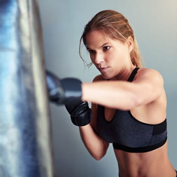 Find the fighter in you. a female boxer training with a punching bag.