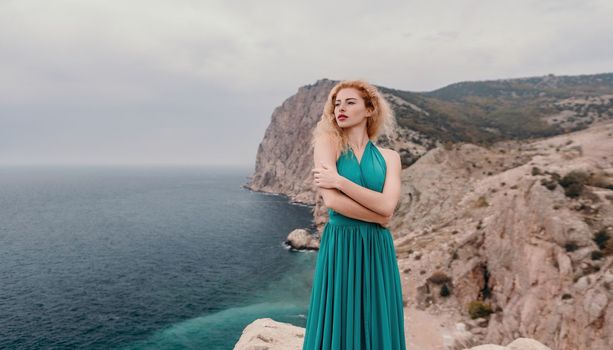 Redhead woman portrait. Curly redhead young caucasian woman with freckles looking at camera and smiling. Close up portrait cute woman in a mint long dress posing on a volcanic rock high above the sea