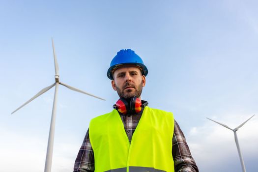 Maintenance worker standing at wind turbine farm looking at camera. Renewable energy.