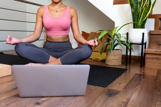 Unrecognizable young woman meditating at home with online video meditation lesson using laptop.