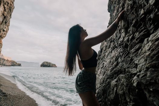 Sports Woman Climbing The Rock. Young woman With slim fit body climbing in volcanic basalt cave with beautiful sea view. The athlete girl trains in nature. Woman overcomes difficult climbing route.