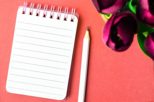 An open spiral bound notebook with lined paper and pencil with red tulip flower on red background.