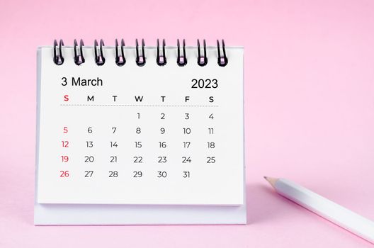 The March 2023 desk calendar for 2023 year and wooden pencil on pink color background.