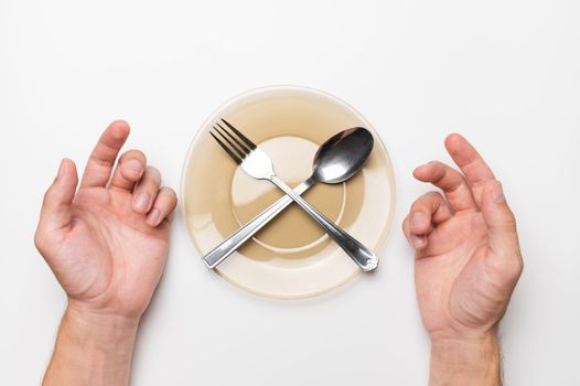 Male hands, an empty plate with a fork and a spoon on a white background, top view. Hunger and food delivery concept