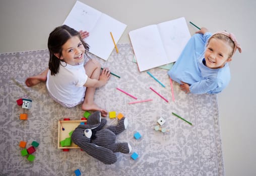 Adorable little girls drawing with colouring pencils at home from above. Carefree girls bonding while playing together. Sisters doing homework together