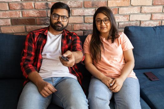 Happy young indian couple relaxing and watching TV at home - leisure and movie and diversity concept