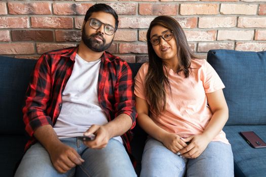 Happy young indian couple relaxing and watching TV at home - leisure and movie and diversity concept