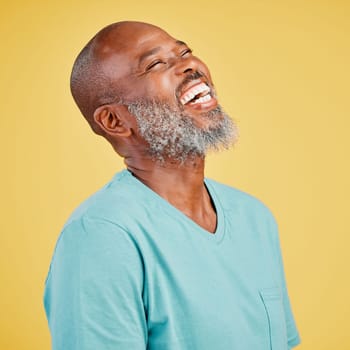 Mature african man laughing out loud against a yellow studio background. Black guy giggling and reacting with laughter while looking cheerful and happy. Lighten the mood with an amusing and funny jok