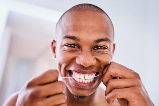 Healthy teeth, now thats something to smile about. an attractive young man flossing his teeth in the bathroom at home