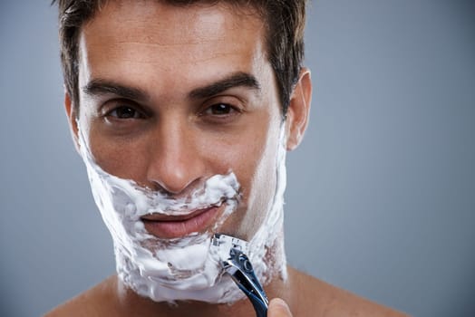 Getting the closest shave ever. Head and shoulders studio shot of a young man shaving.