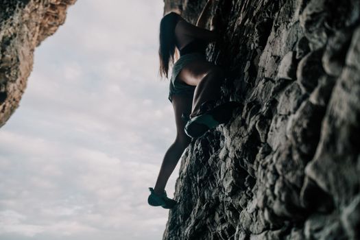 Sports Woman Climbing The Rock. Young woman With slim fit body climbing in volcanic basalt cave with beautiful sea view. The athlete girl trains in nature. Woman overcomes difficult climbing route.