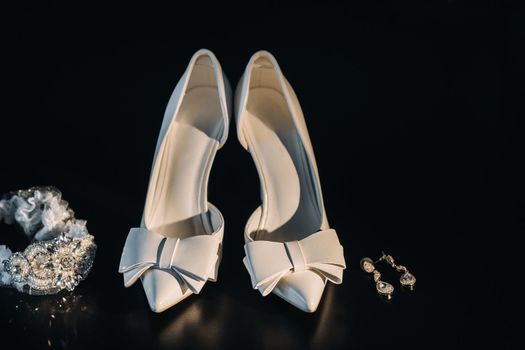 white wedding shoes and garter belt with earrings on a black background