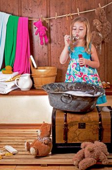 Fun home photo session. Curious little girl washes bears in an antique copper basin with water and soap suds at home